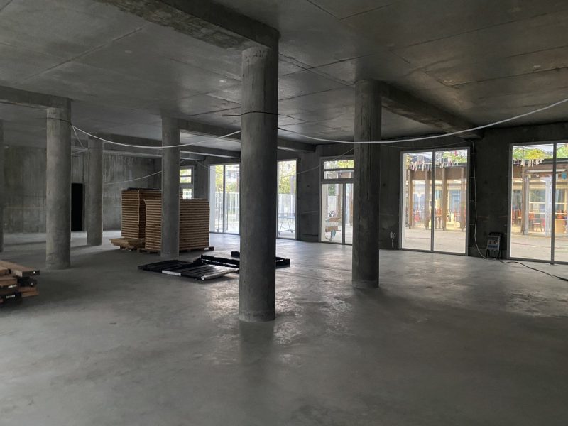Espace intérieur brut en béton avec poteaux cylindriques, plafond apparent et grandes baies vitrées donnant sur l'extérieur