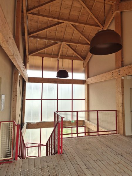 Mezzanine en bois avec garde-corps métallique rouge, charpente apparente et grande baie vitrée à cadre rouge