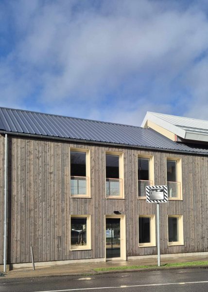 extrait de la façade de l'extension avec bardage bois vertical et menuiseries aluminium claires sous un ciel bleu